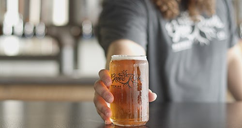 Close up of a bartender holding a cold glass of beer with the Grove Roots Brewing Company Logo on it - Grove Roots glass -  provided by Winter Haven Chamber of Commerce