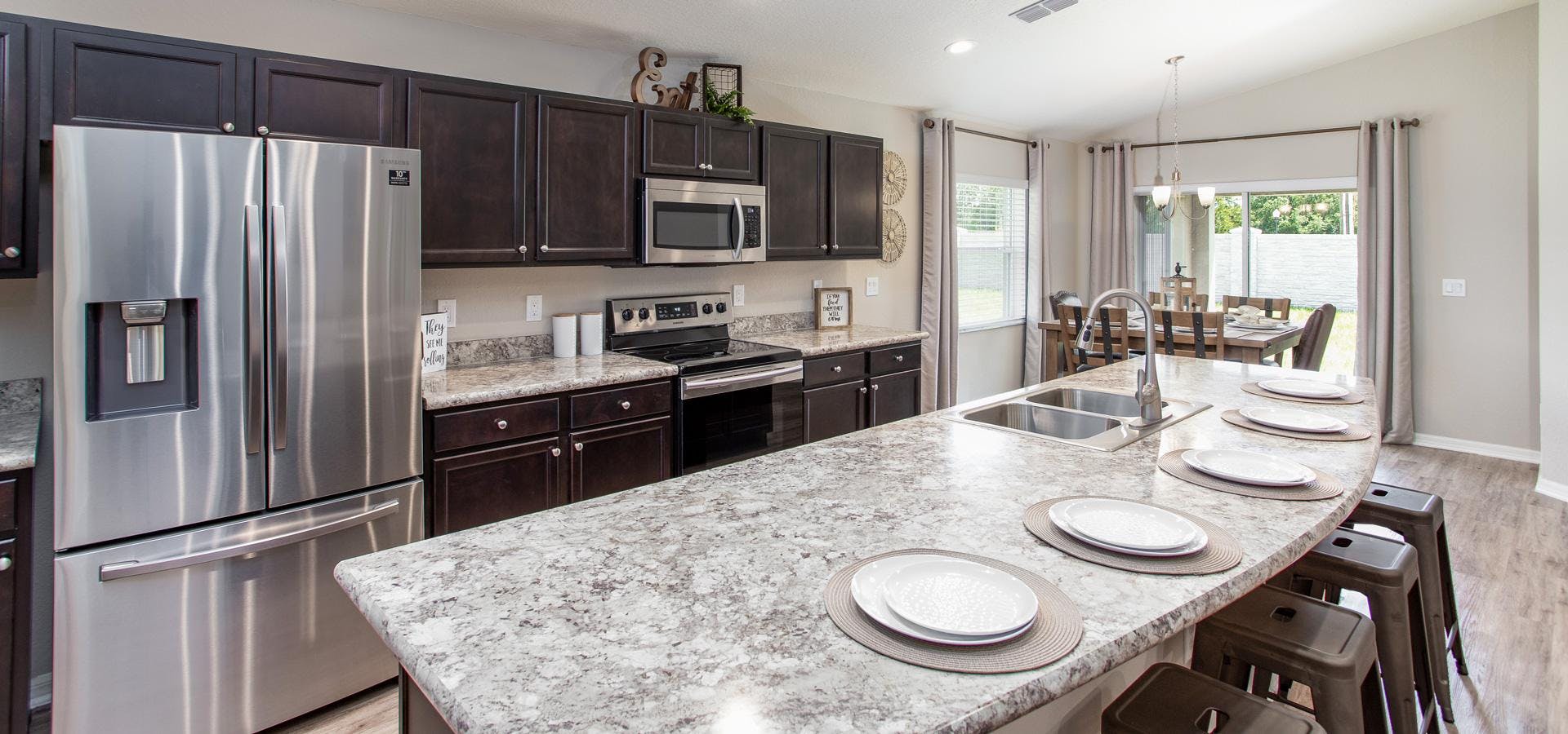 Open kitchen with espresso cabinets and stainless steel appliances and sunny cafe area in the Raychel, a new home plan by Highland Homes