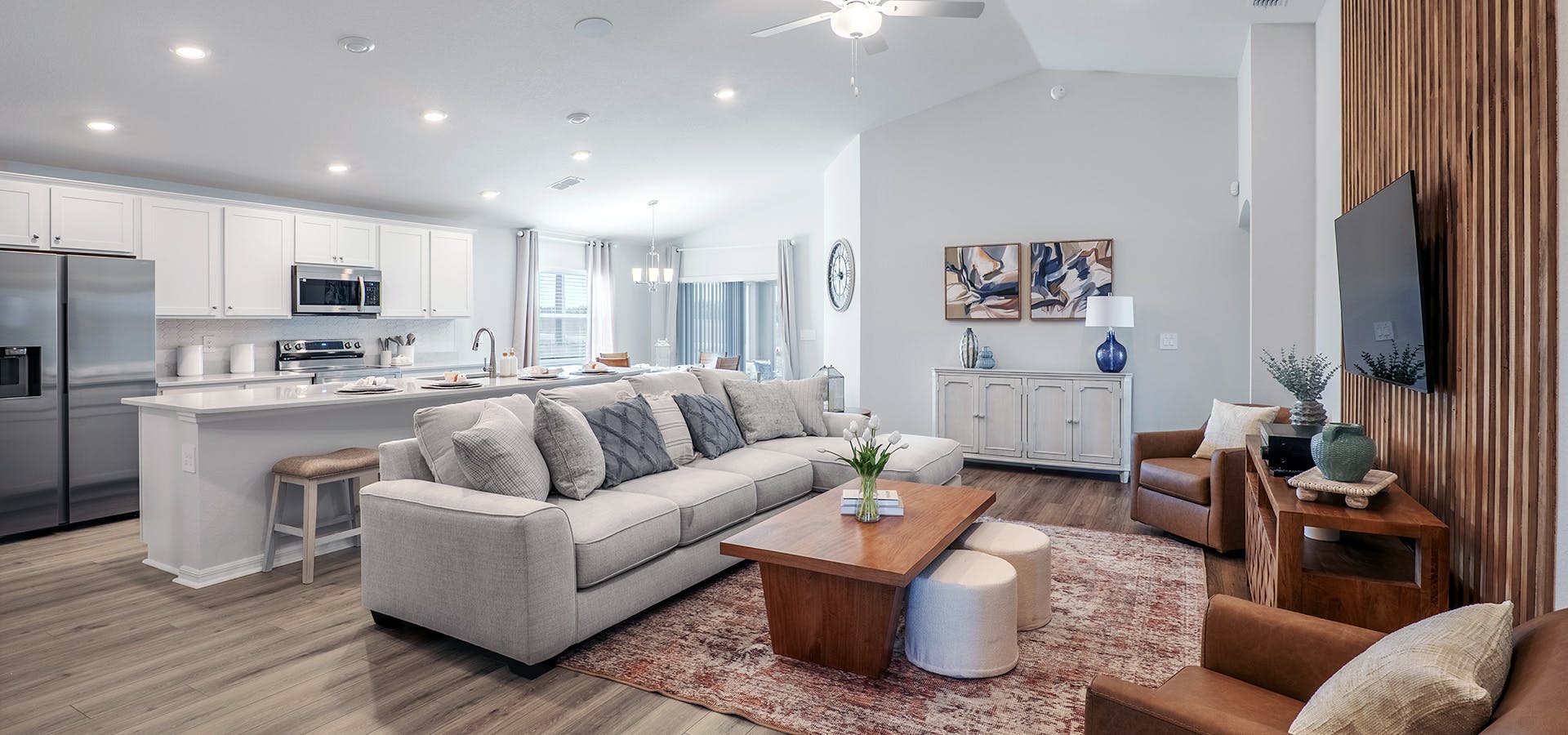 An open living area with wood accents, a large sectional, leather armchairs, and open island kitchen.