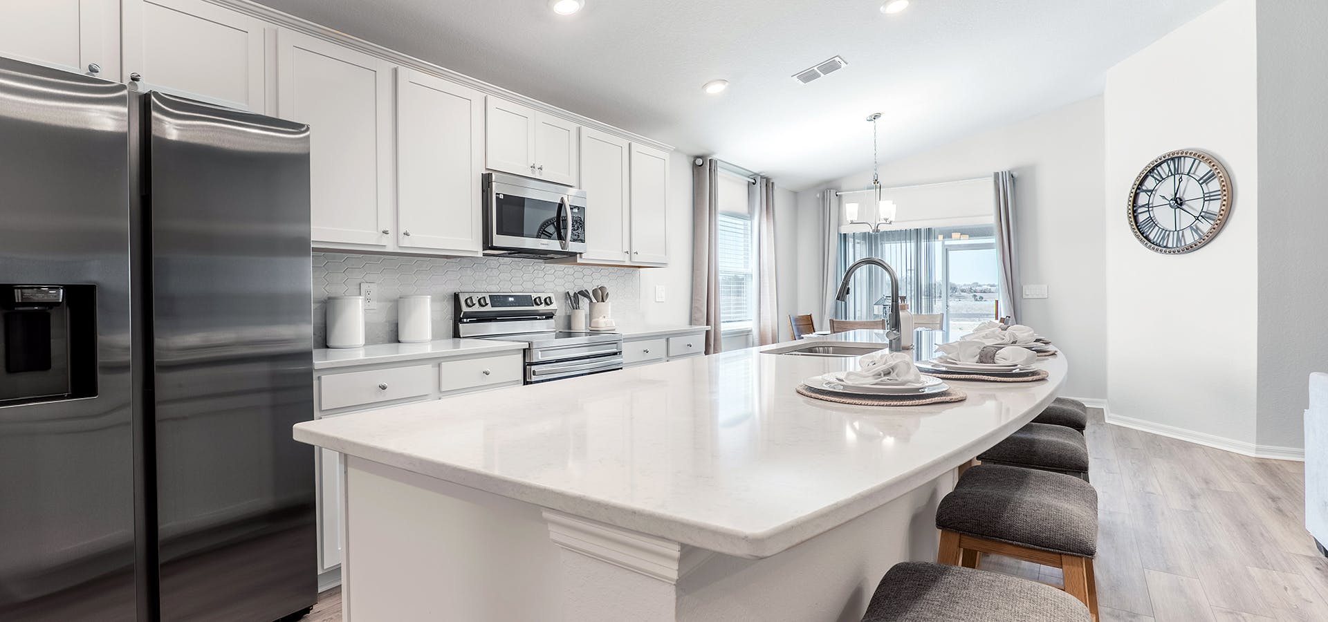 Kitchen with a large island, white cabinets, quartz, and SS appliances.