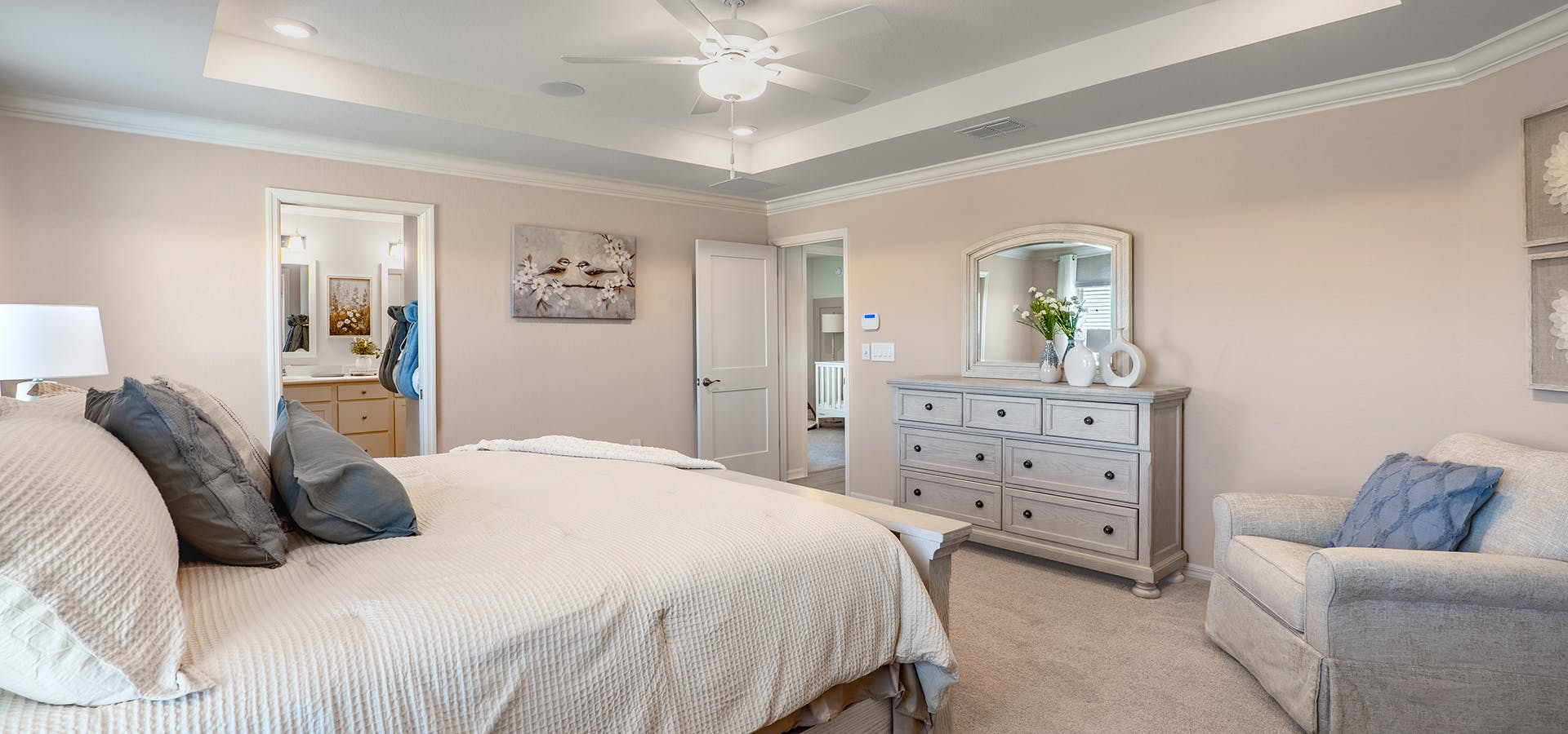 A large primary bedroom suite with creamy neutral colors and an overstuffed armchair,