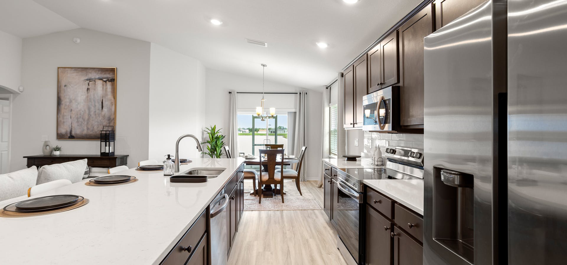 Sunny, open kitchen with dark wood cabinets, light colored quartz countertops, and eat-in space.