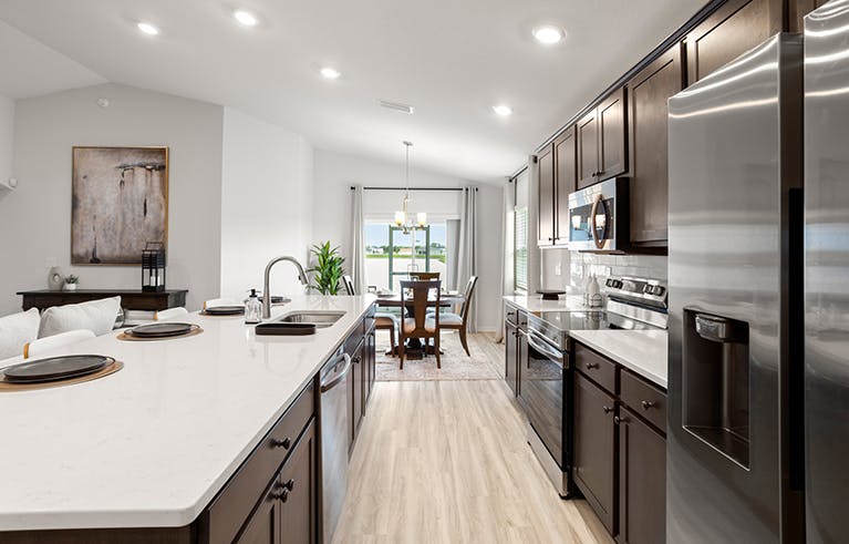 Sunny, open kitchen with dark wood cabinets, light colored quartz countertops, and eat-in space.