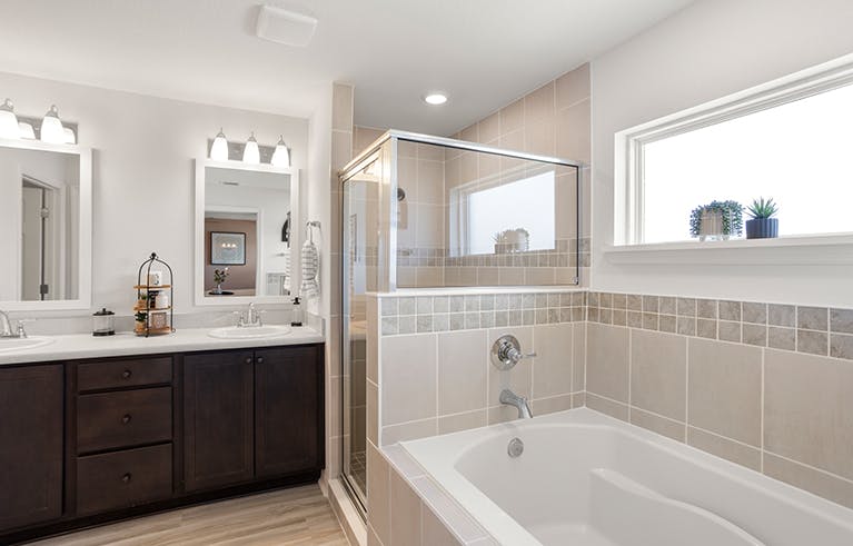 A tiled garden tub, tiled shower, and wood vanities in a large bathroom.