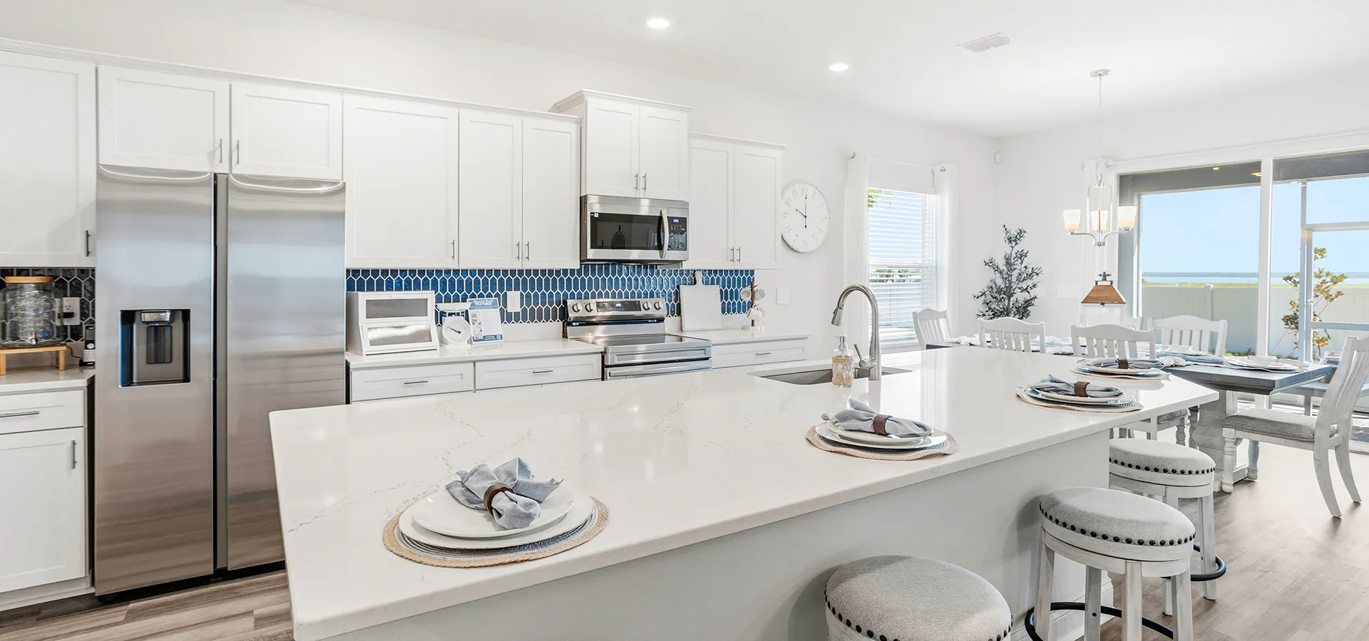 Bright, open kitchen in the Shelby II by Highland Homes, with a large island, quartz counters, white staggered cabinets, and a blue tiled backsplash.
