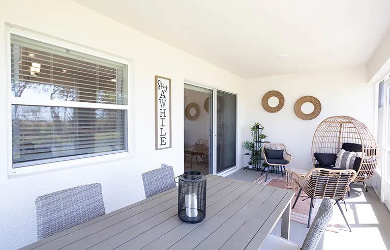 A large screened lanai on a Florida new construction home, with an outdoor table and wicker papasan chair.