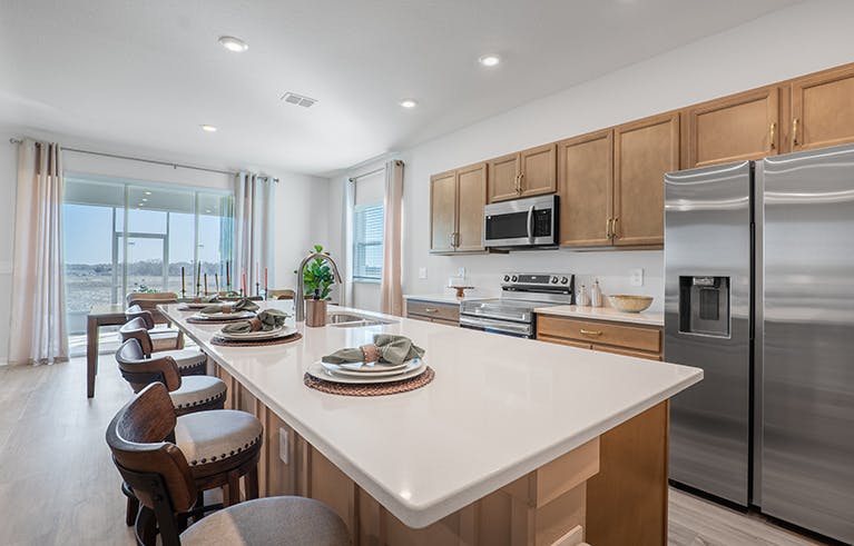 Kitchen with a large island, wood cabinets, quartz counters, and a triple sliding glass door opening to outdoor living space.